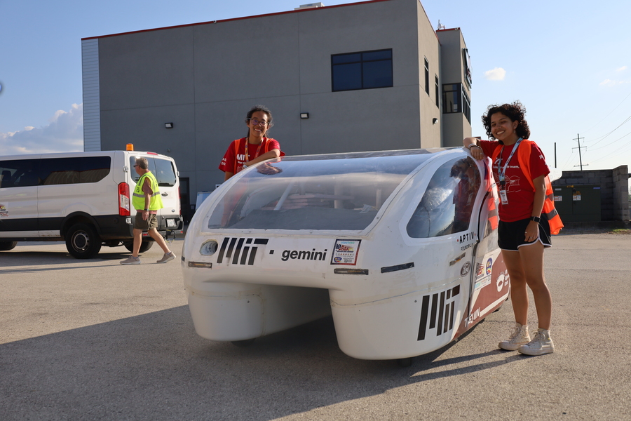 Adrienne Lai and Tessa Uviedo, in matching red shirts, pose standing on either side of a solar electric vehicle