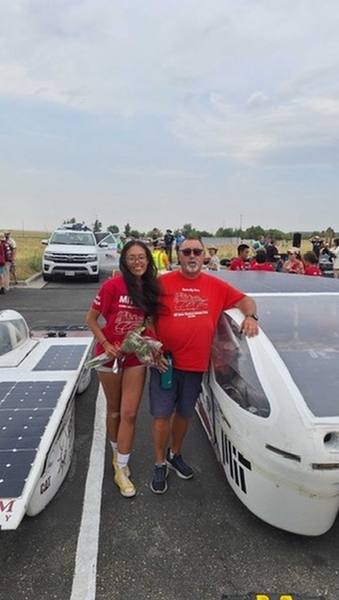 drienne Lai and Pat McAtamney, in matching red T-shirts, stand between two solar vehicles in a parking lot