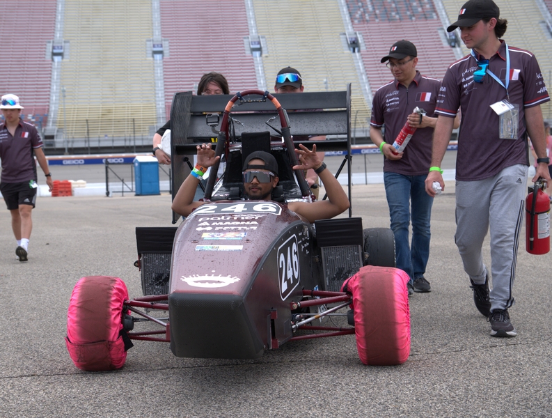 Faris Elnager sits in the cockpit of a Formula-style race car surrounded by team members