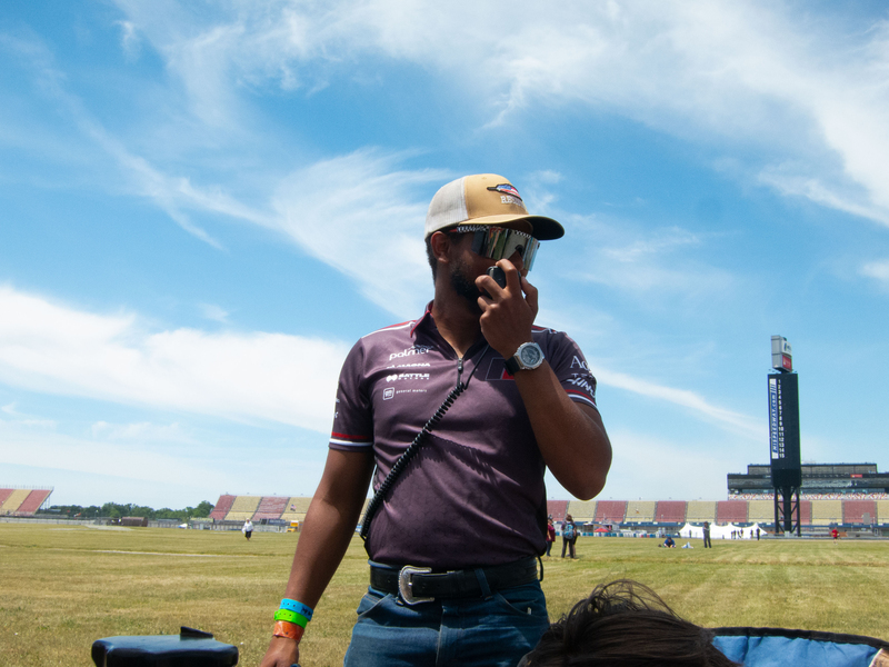 Faris Elnager stands in a field, speaking into a walkie-talkie, his face obscured by safety glasses and shade
