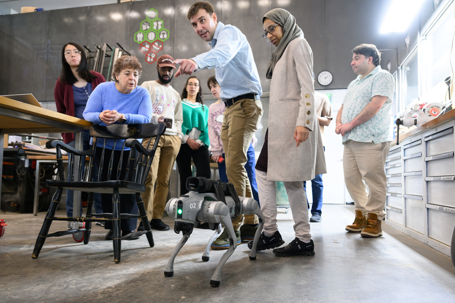 A man uses a remote control to operate a robot dog in the workshop classroom as attendee look on.