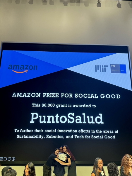 Three women pose in front of a screen announcing that PuntoSalud has won a $6,000 grant.