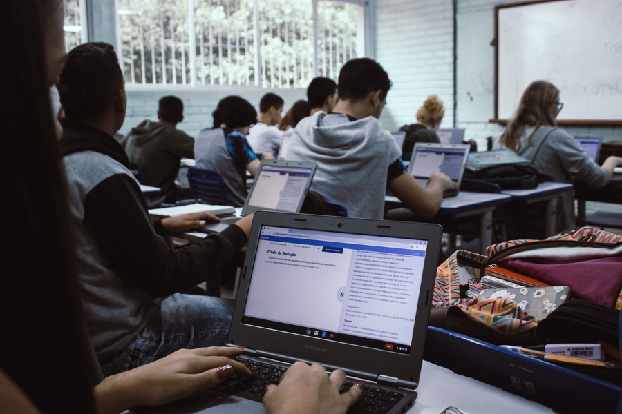 Group of high school students pictured sitting at desks with their back to the camera, typing on laptops