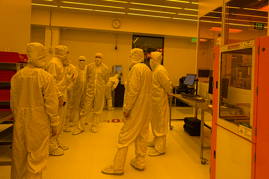 Eight people wearing bunny suits stand inside MIT.nano's golden-lit cleanroom.