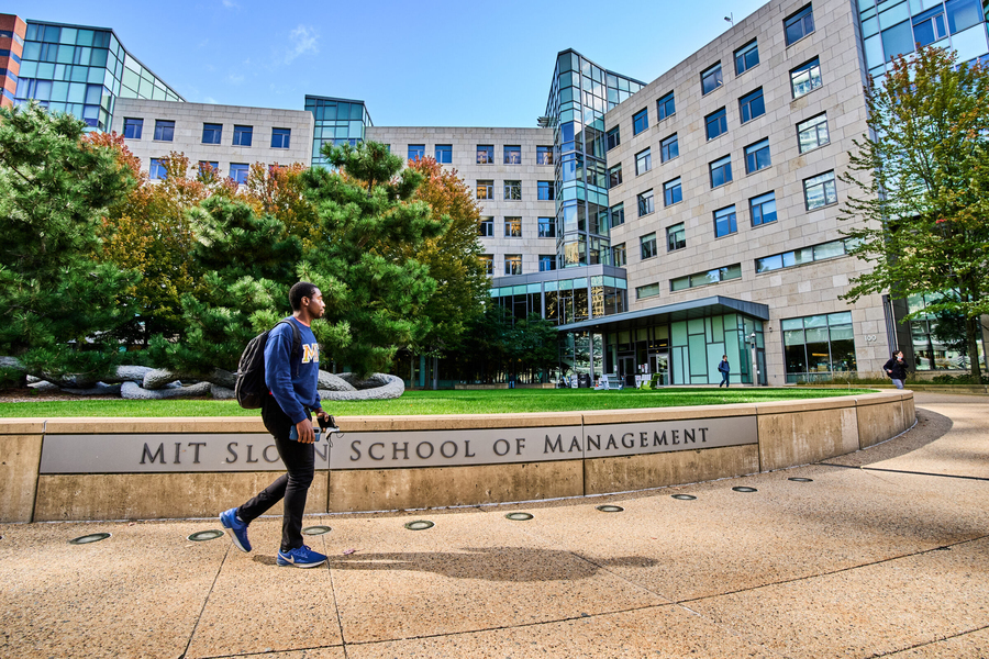 Student walks by the MIT Sloan School of Management sign out front of building E62 on a sunny day