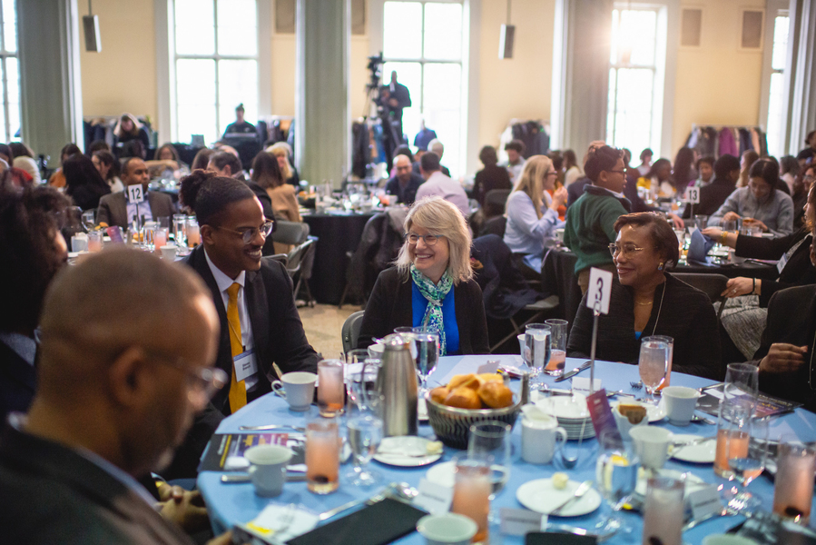 Sally Kornbluth, Paula Hammond, and others chat at a round table with other tables in the background