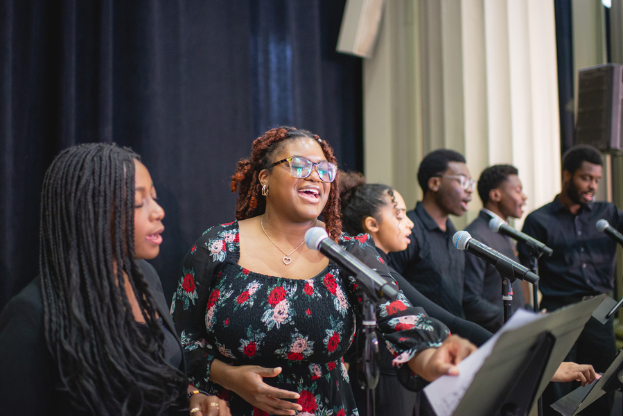 Six MIT Gospel Choir members stand before microphones, singing