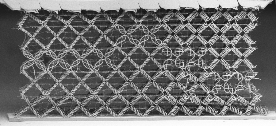 A black and white image of a woven metamaterial, comprised mostly of diamond-shaped cells woven from spiral fibers