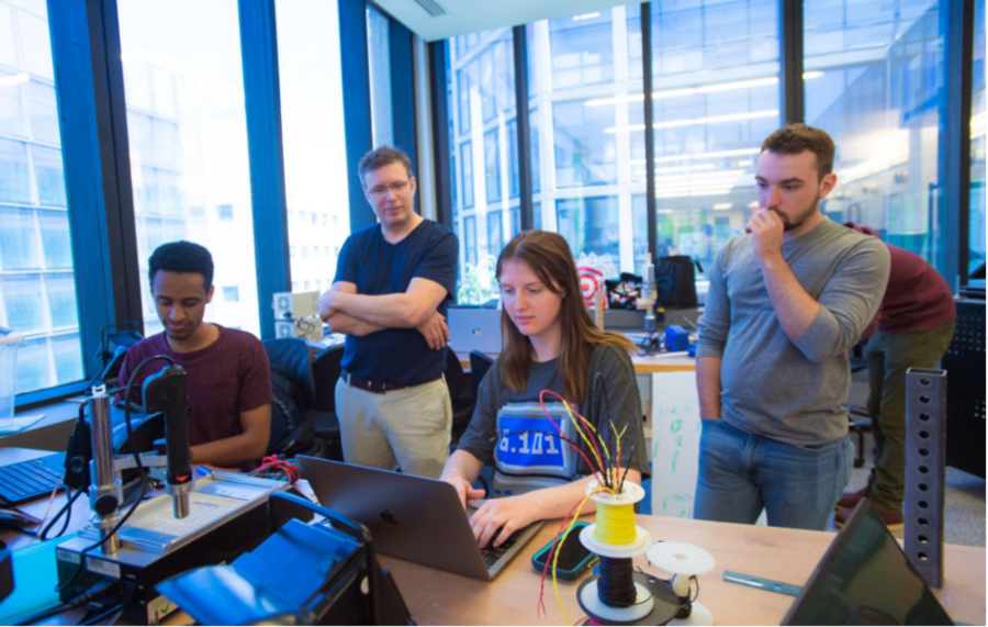 Two men stand behind two students seated at a table