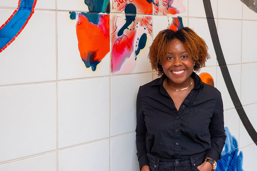 Zuri Sullivan leans against white tile wall painted with a colorful abstract design