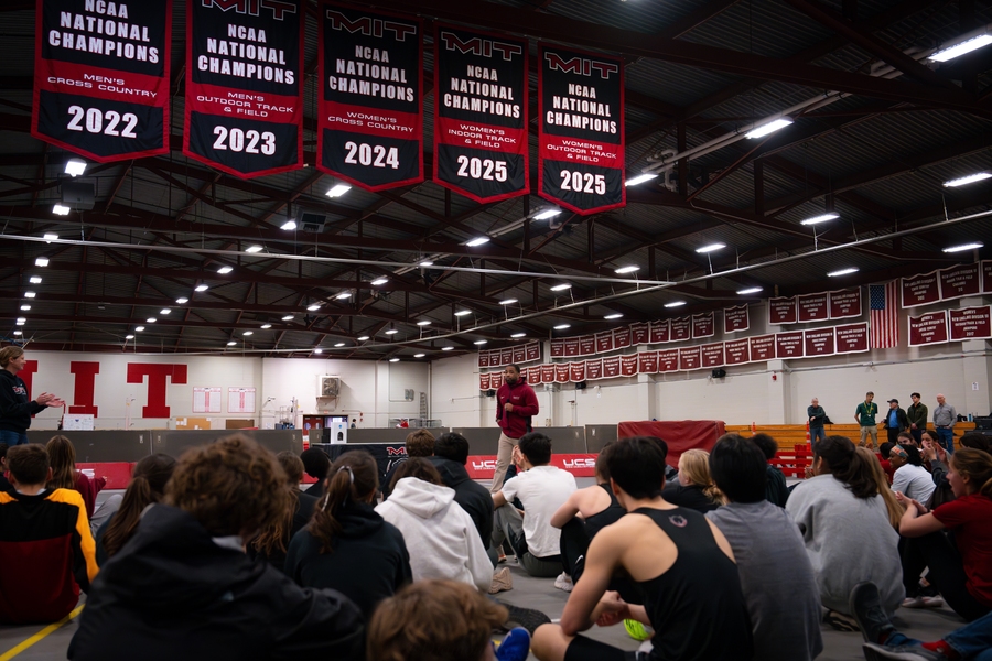 G. Anthony Grant speaks in a gym filled with MIT sports banners to students seated on the floor.