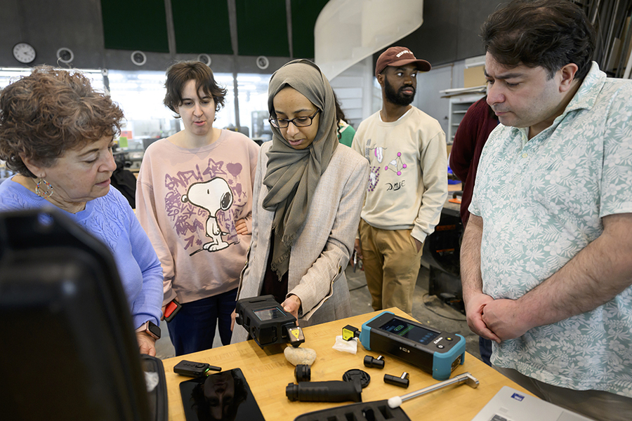 Lamyaa Almehmadi displays a handheld device to attendees standing around a small table