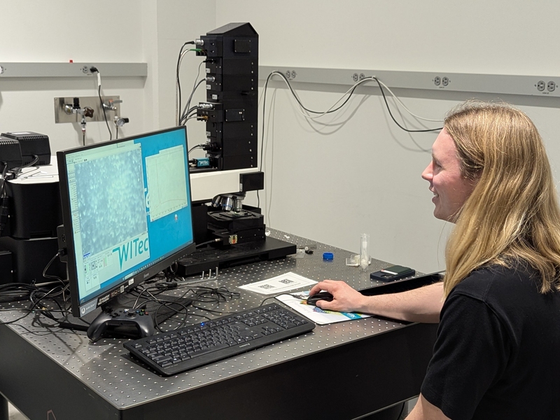 David Lundberg sits in front of a computer screen next to a microscope.