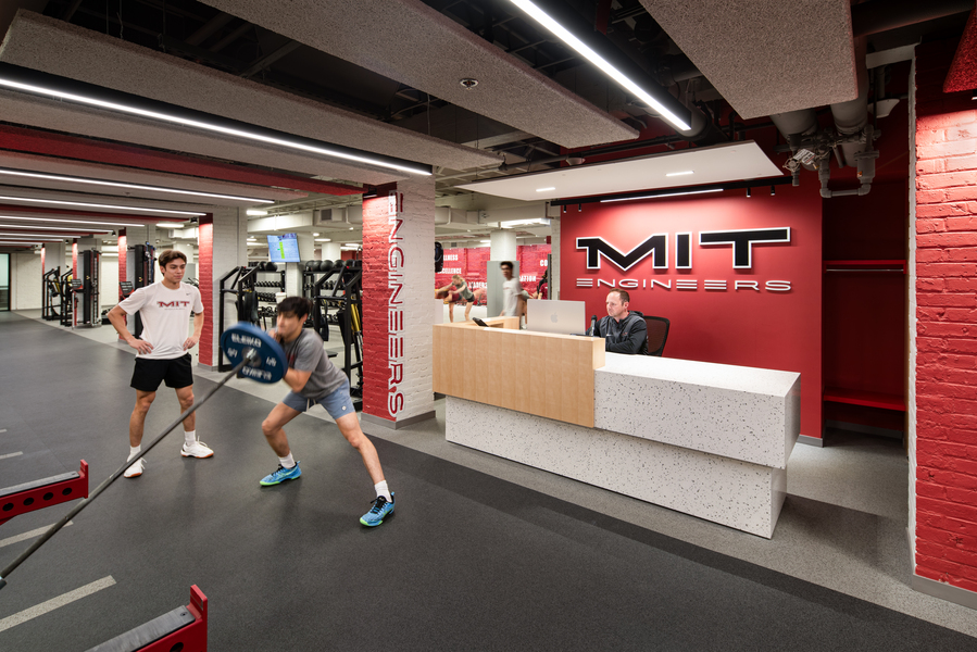 Photo of the MIT Sports Performance Center with a few students exercising and a man seated at a desk