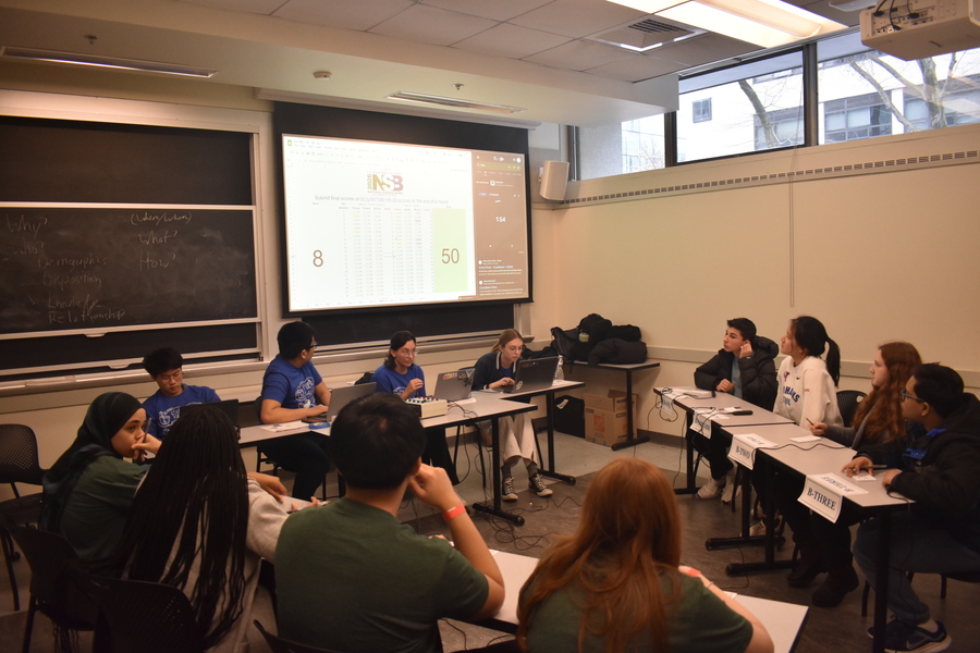 12 people sit at three tables arranged in a triangle in a classroom.