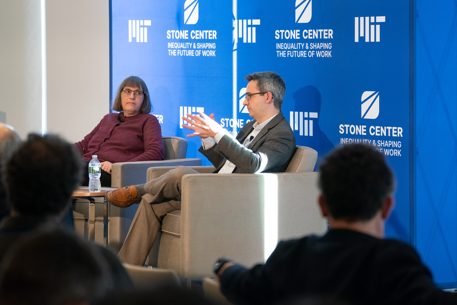 Elizabeth Anderson and Oren Cass sit in armchairs on stage in front of a blue Stone Center banner.