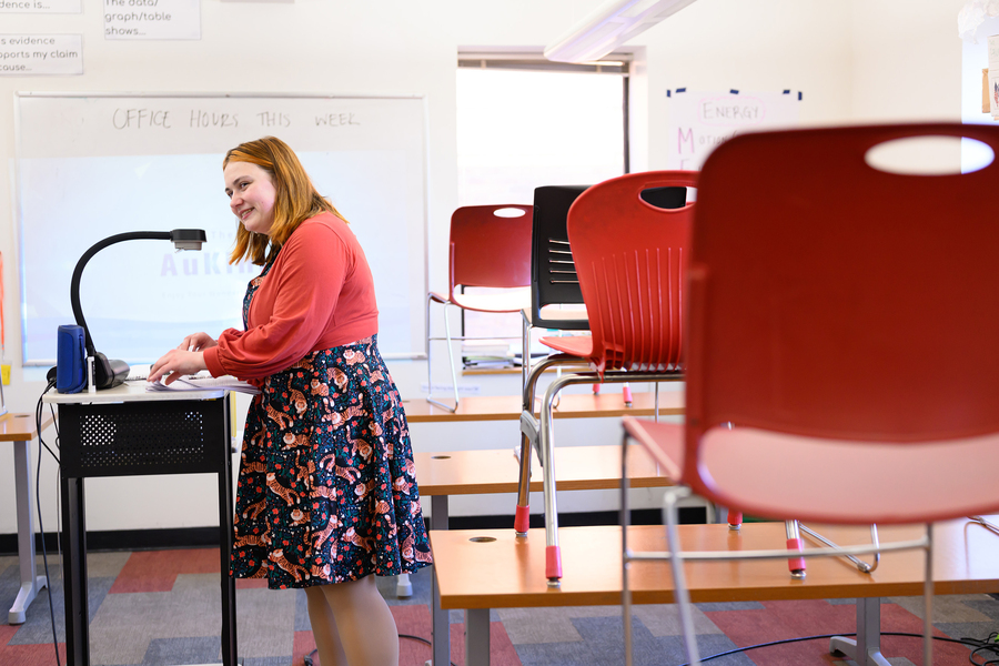 Nik Sandu stands before a projector in a middle school classroom. The desks have chairs atop them.