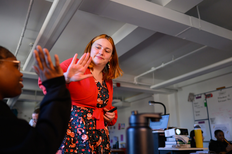 Standing, Nik Sandu gives a seated student a high five in her seventh-grade classroom.