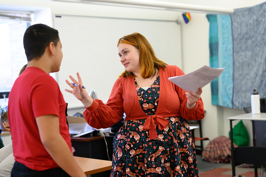 Holding a stack of papers, Nik Sandu talks with a seventh-grade student in their classroom.