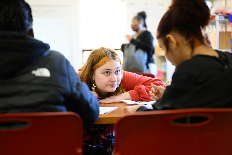 Nik Sandu crouches down in front of a desk to talk with a student
