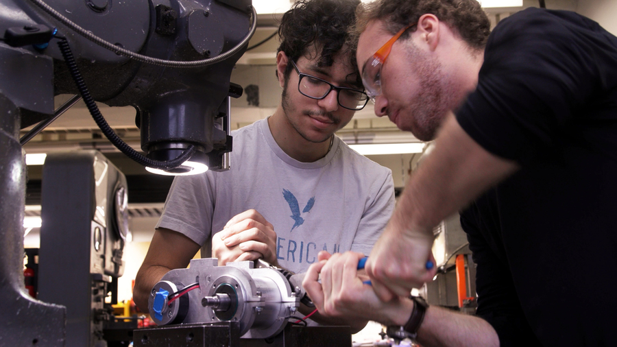 Two students wearing safety glasses look at a lathe they've assembled 