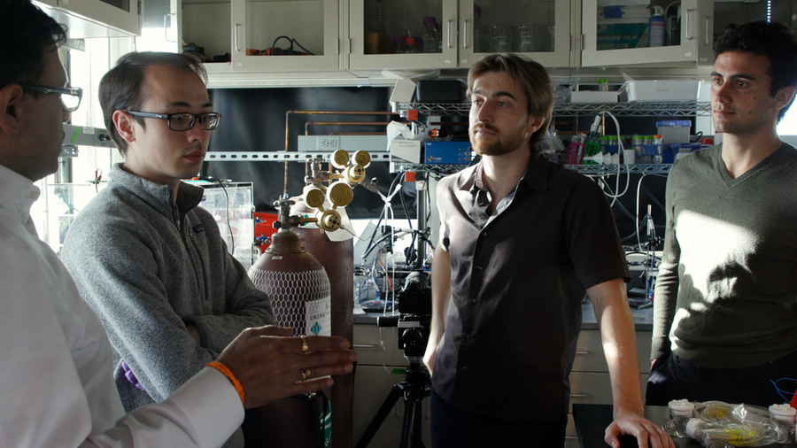 Four men stand in a half circle, talking, in a lab at MIT 