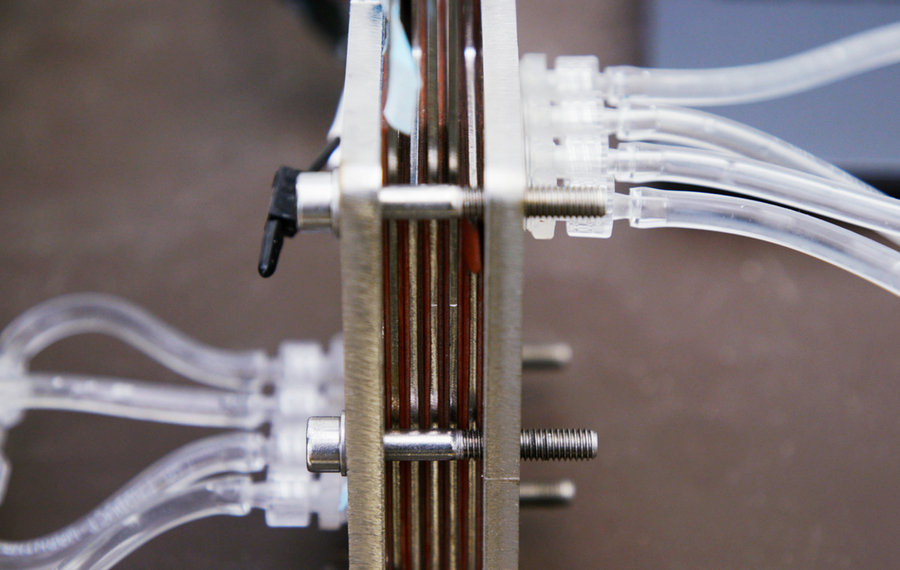 Extreme closeup of a mechanical device used to buffer river water, comprising several flat plates bolted together with tubes extending on each side