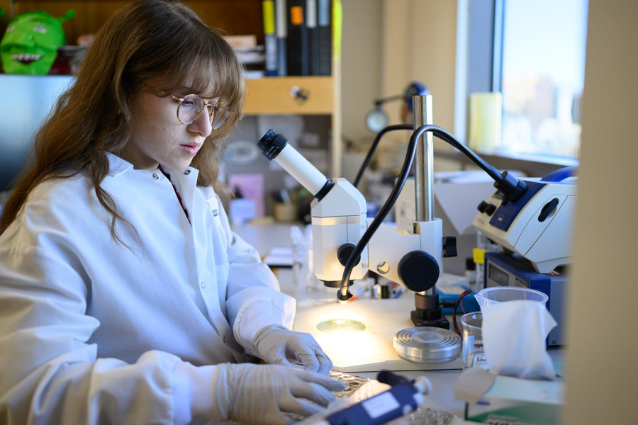 Giselle Valdes, wearing a lab coat and nitrile gloves, works at a lab bench.
