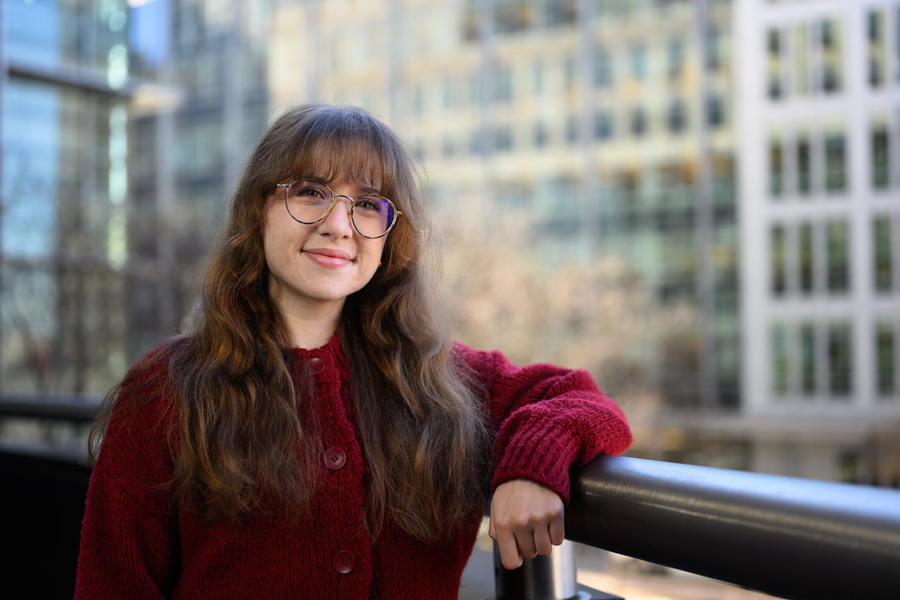 Giselle Valdes poses leaning on a railing, with large office buildings in the background