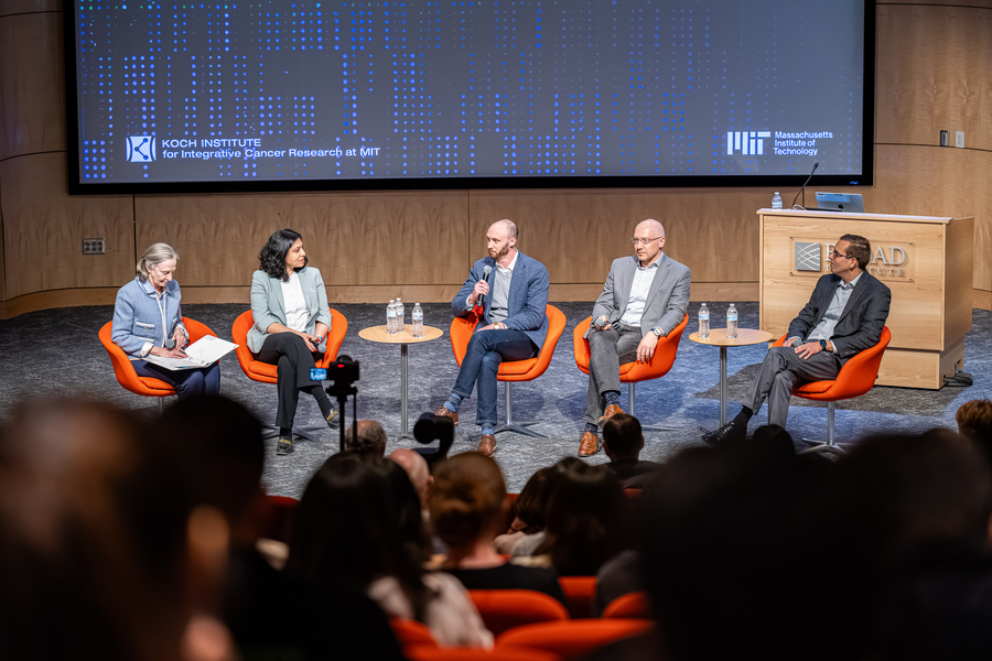 5 people seated in orange chairs on an indoor stage