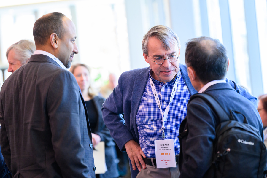 A man wearing a lanyard speaks to two others whose backs are to the camera