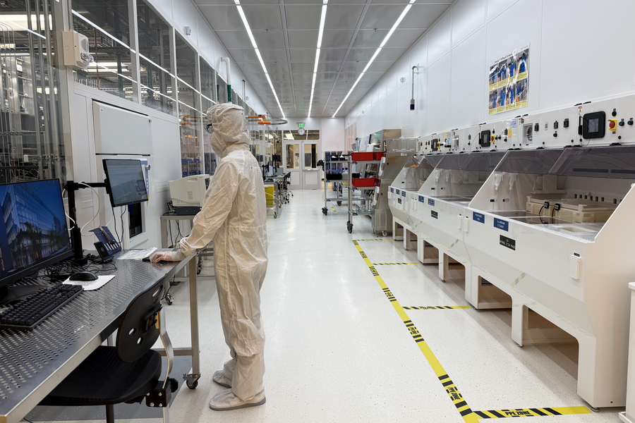 A person in a bunny suit stands at a computer in a cleanroom.