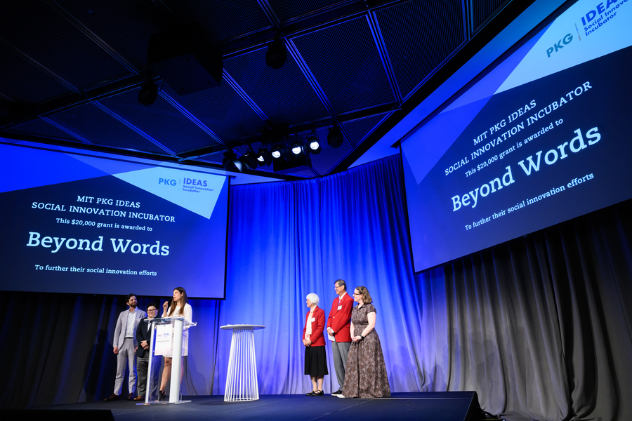 Six people stand on a stage under two screens displaying their team name, Beyond Words