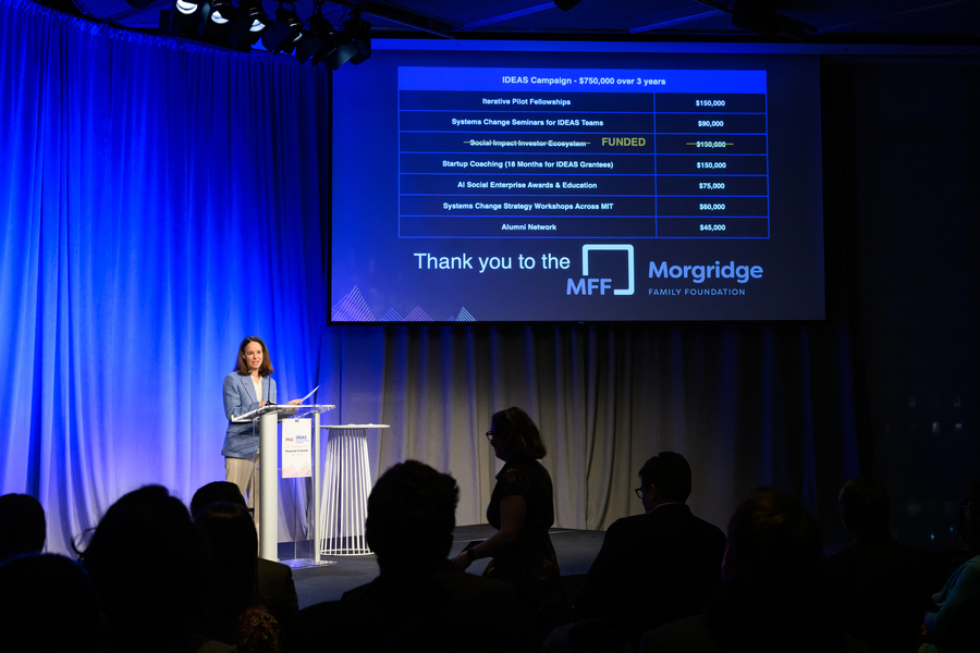 Alison Badgett at a lectern on an indoor stage, under a projected list of PKG Center funding priorities.