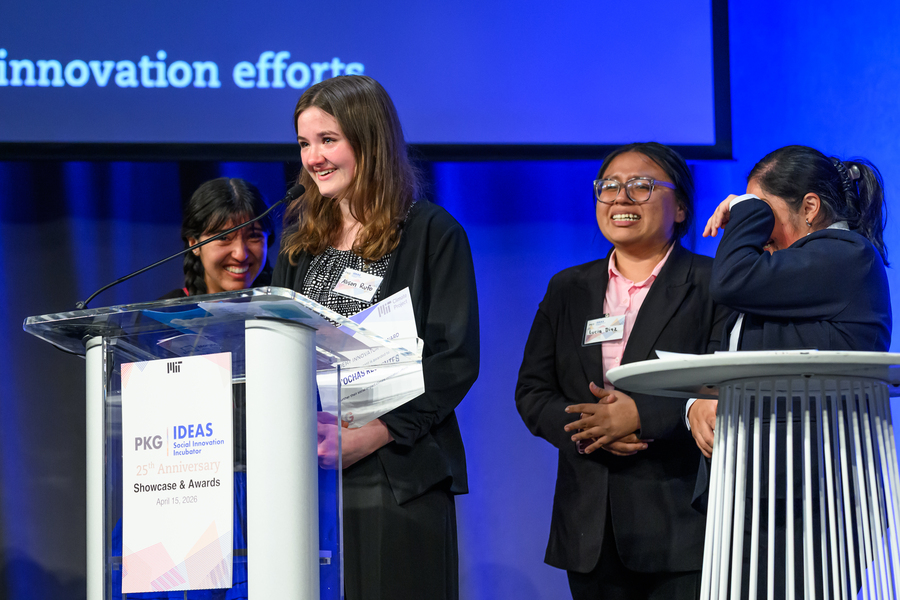 Four young women, some with tears in their eyes, stand at a lectern on an indoor stage to accept an award