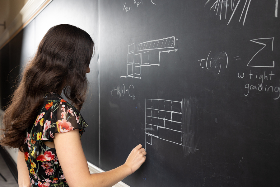 Pictured from her right side, Amanda Burcroff writes equations on a chalkboard.