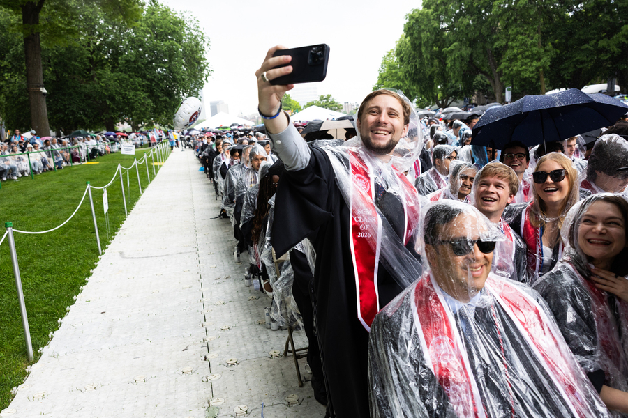 Graduates wear ponchos and one takes a photo
