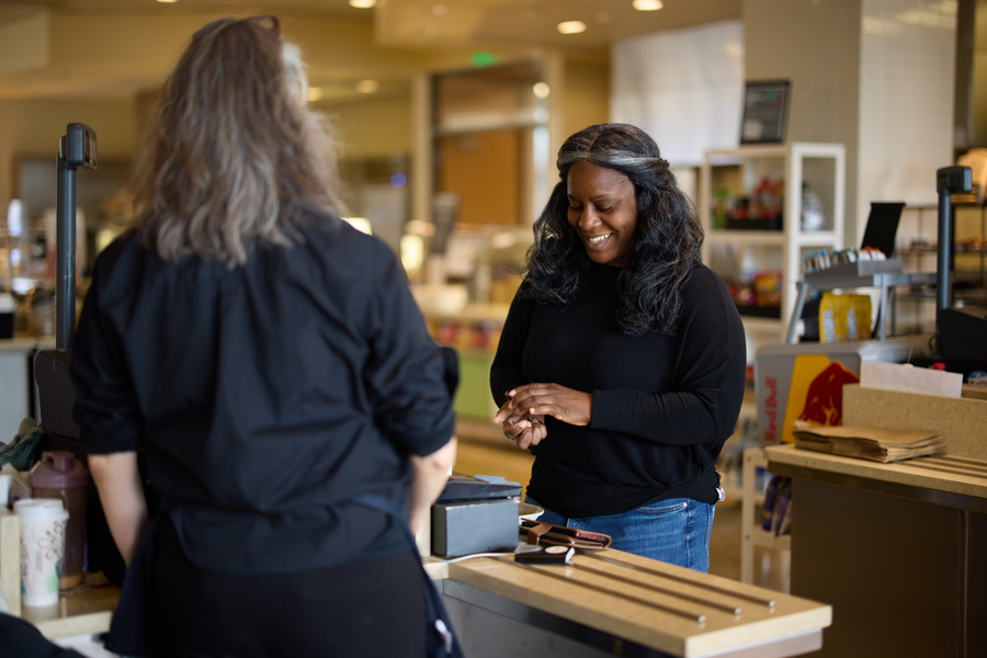 Alecia Asiamigbe, facing a cash register, pays for a purchase in a small cafeteria