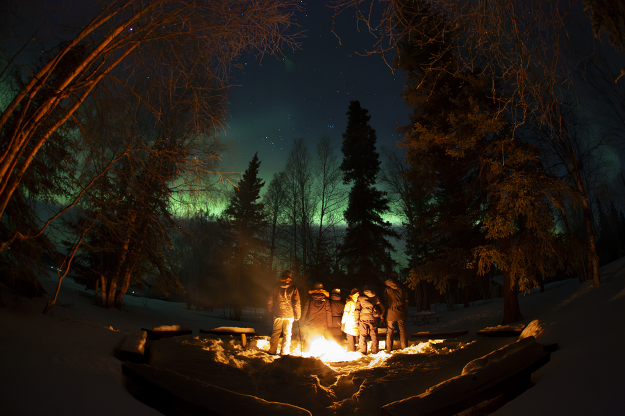 Group of people standing around a fire outdoors at night, taken with an all-sky camera that greatly distorts the borders