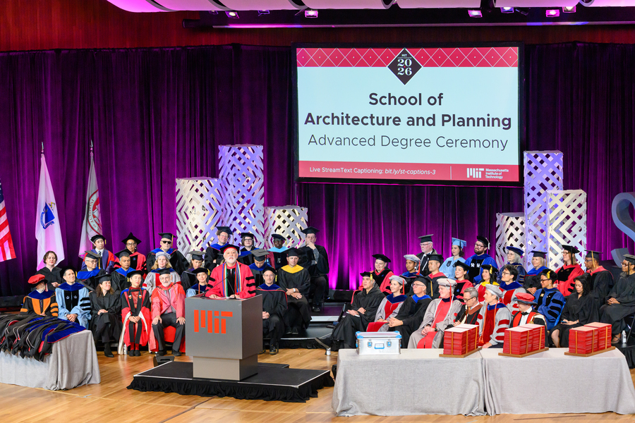 Wide view of the Kresge Auditorium stage shows faculty in graduation regalia seated behind a podium as Hashim Sarkis addresses graduates.