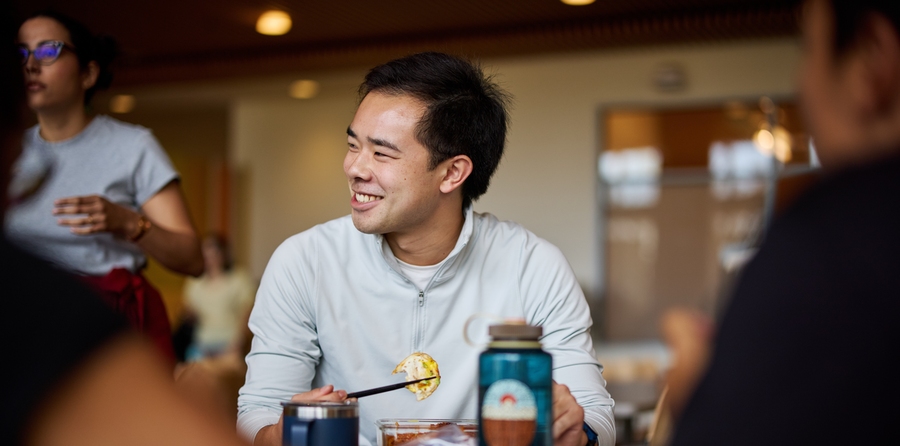 Patrick Yeung sits in a cafe, eating sushi and smiling at friends outside of the frame