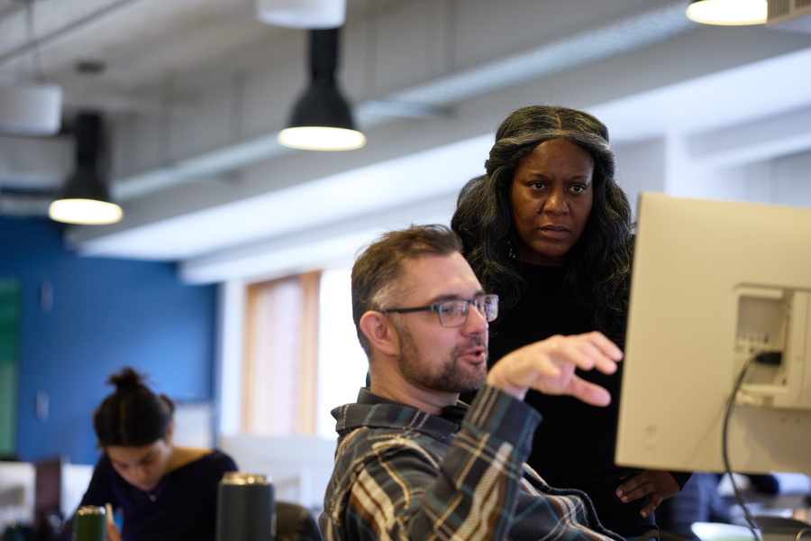 A man points at a computer screen while Alecia Asiamigbe looks over his shoulder, listening to him speak.