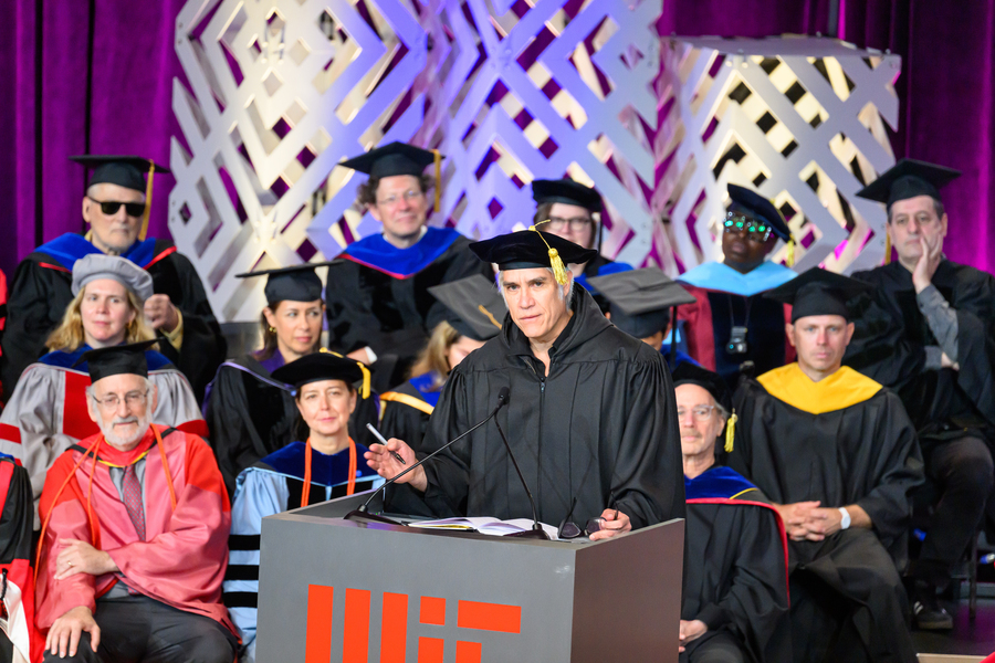 Alejandro Aravena stands at an indoor MIT lectern. MIT faculty members sit behind him. All wear academic regalia.