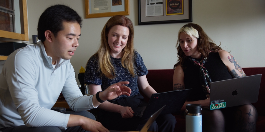 Patrick Yeung sits on couch with two female colleagues, discussing the information on their laptops 