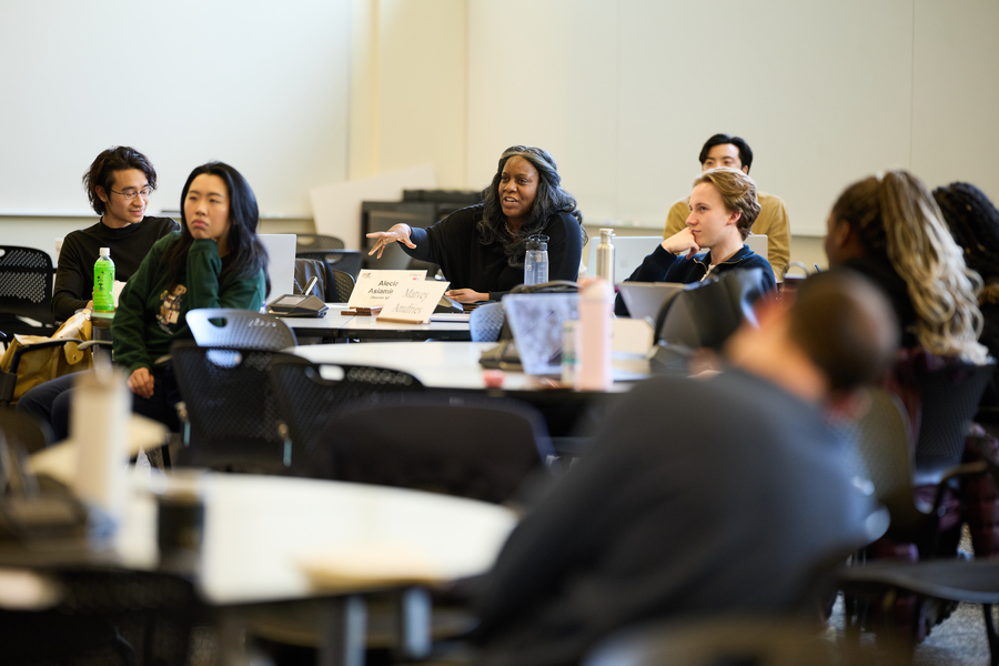 Asiamigbe speaks during a lecture, seated in the middle of a busy classroom, surrounded by other students