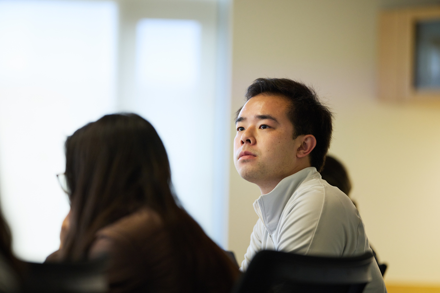 Patrick Yeung sits in a classroom, looking off into the distance, with another student in the frame