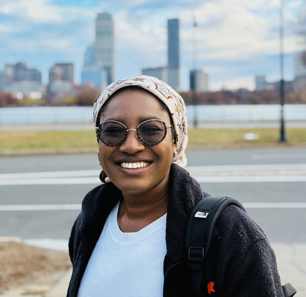 Akorfa Dagadu poses for a photo outdoors, with Boston’s skyline out of focus in the background