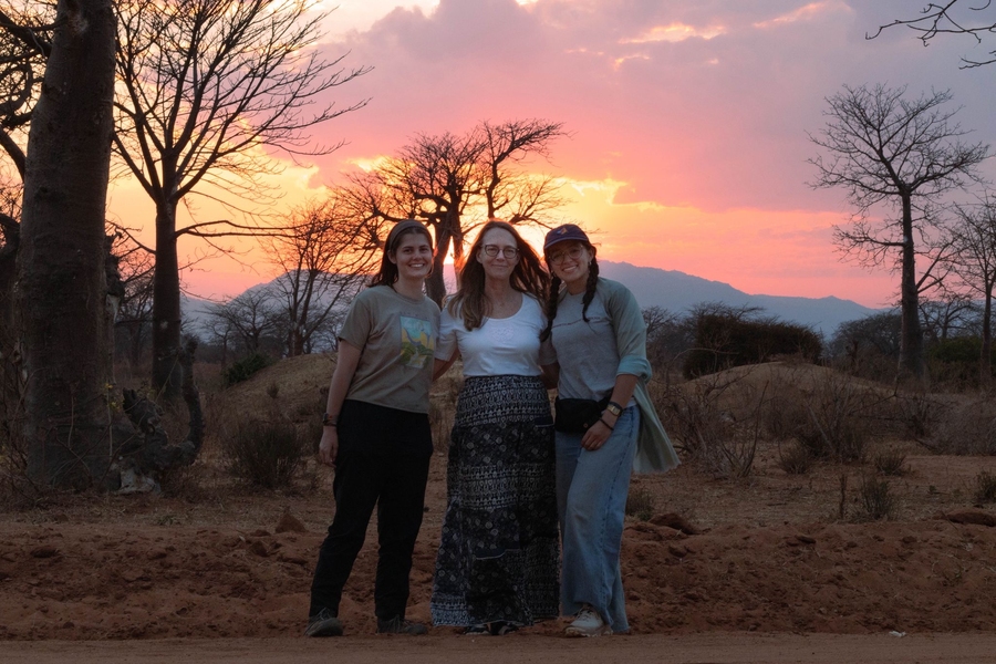 Celestina Pint, Barbara Piper, and Isabel Duran pose before a sunset over a Tanzanian grassland