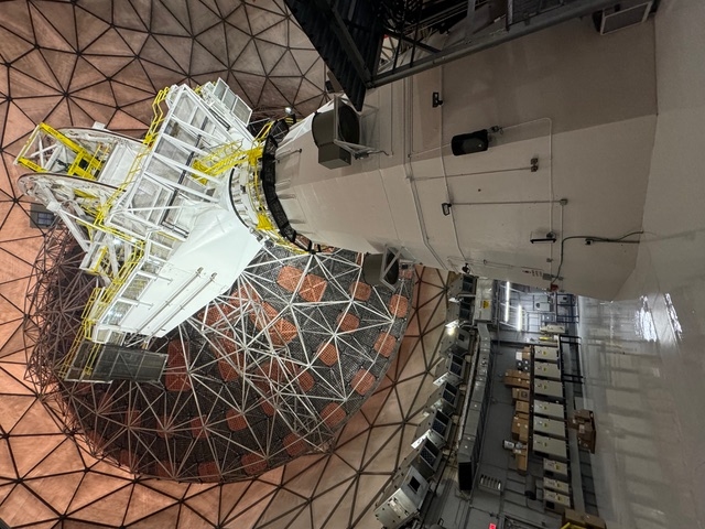 A large radio telescope faces away from the camera, contained within a geodesic dome