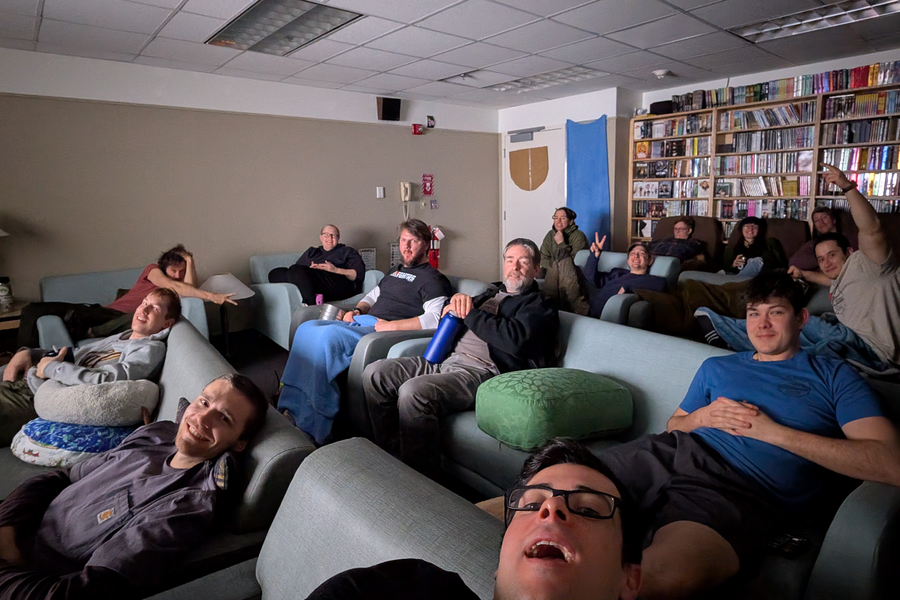 14 people recline on couches, smiling at the camera 